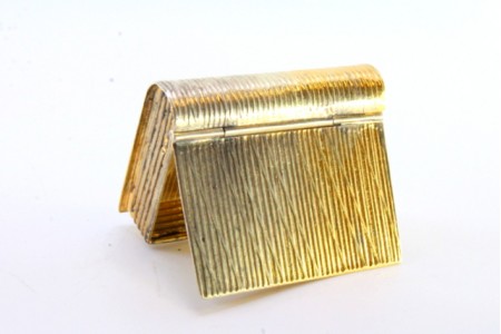 Caixa de comprimidos em prata dourada em forma de livro com tampa basculante.